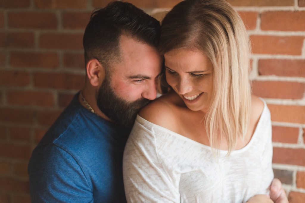 engaged couple cuddling together in front of brick wall