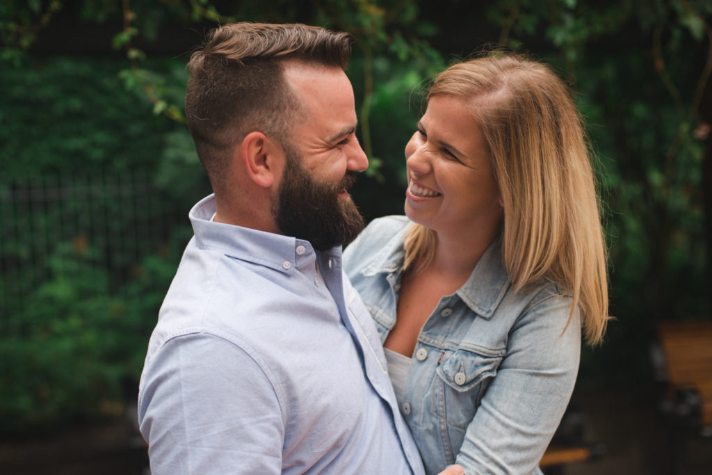 engagement couple looking at each other laughing with green vines in the background
