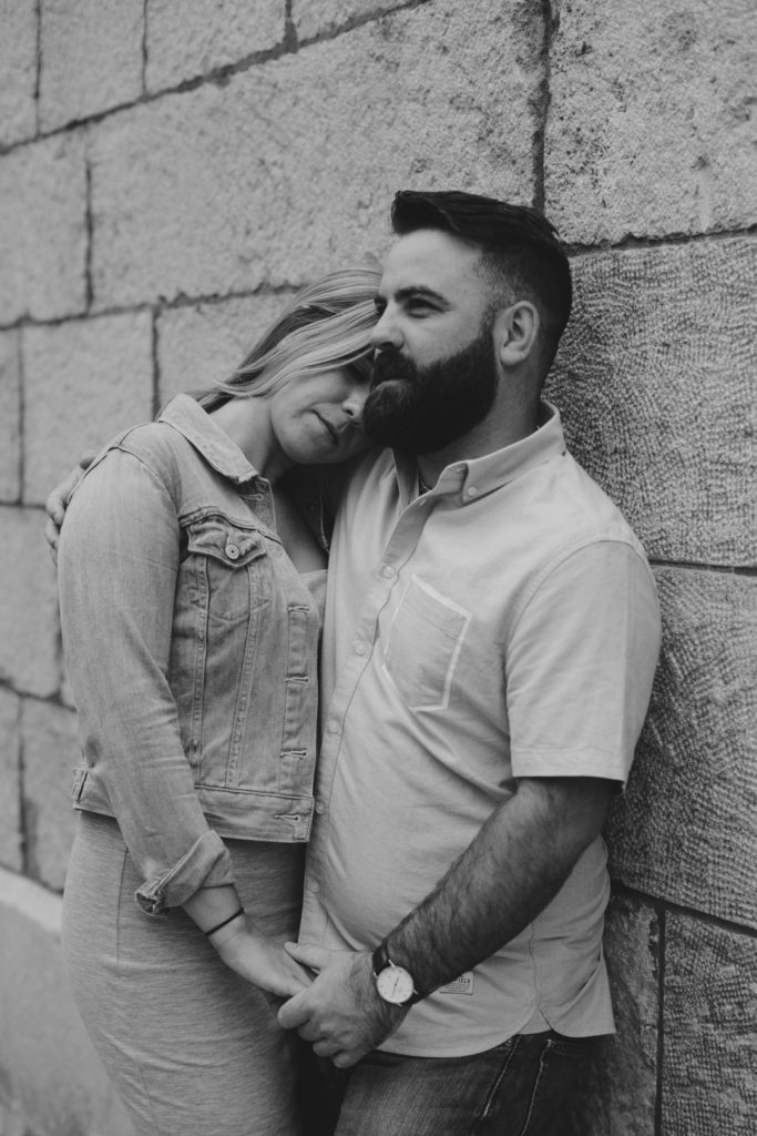 black and white photo of girl resting her head on her boyfriend's shouder as they lean against a brick wall