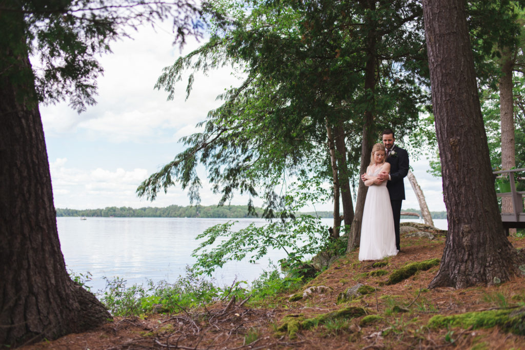 bride and groom cuddling by the water's edge at cottage wedding