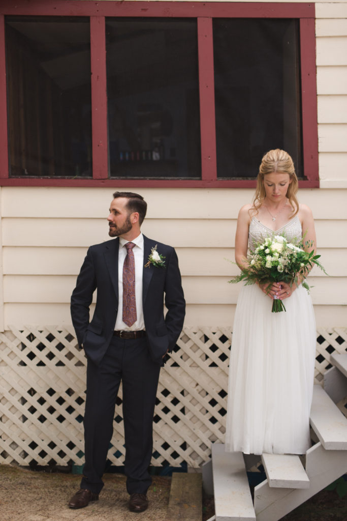 bride and groom standing below red window at the cottage