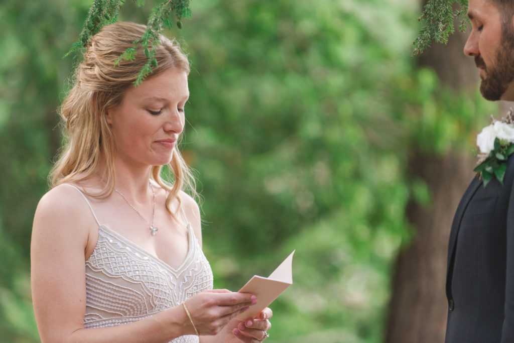 bride reading her vows during wedding ceremony by the lake