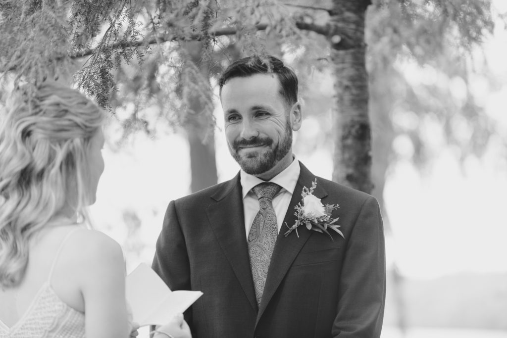 groom smiling as his bride reads her wedding vows to him