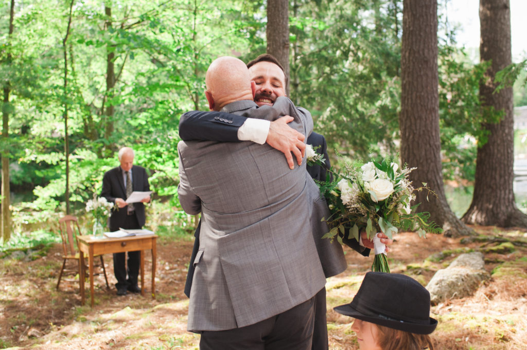 groom hugging his dad holding wedding bouquet after ceremony