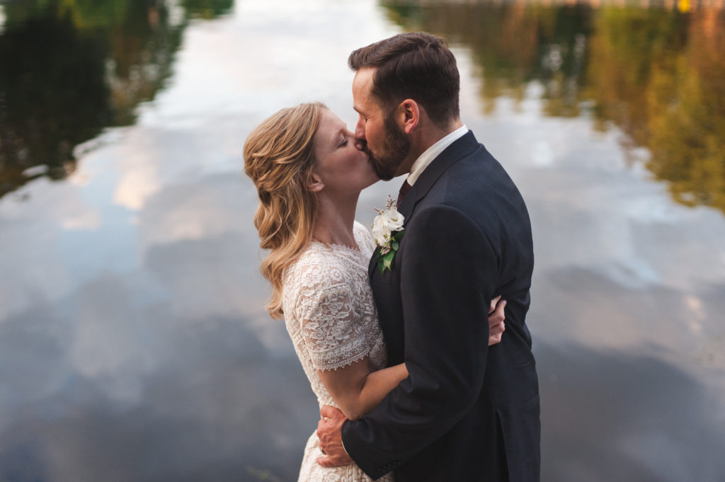 bride and groom kissing with reflection of water and trees in the background