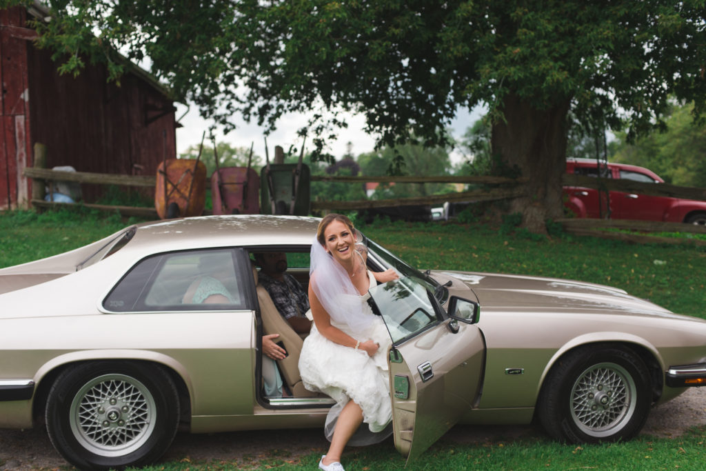 bride getting out of old jaguar on her wedding day