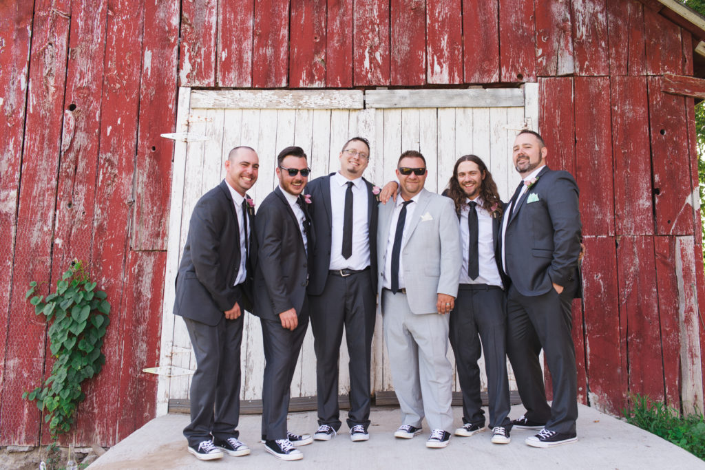 groom and groomsmen in front of red shed wearing black converse shoes