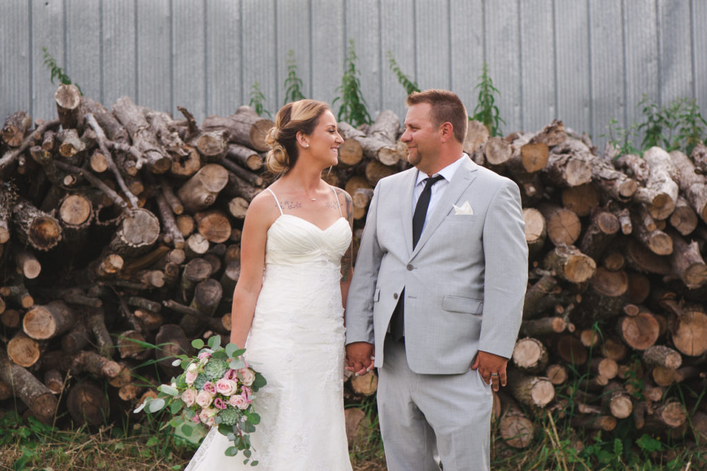bride and groom in front of stacks of wooden logs