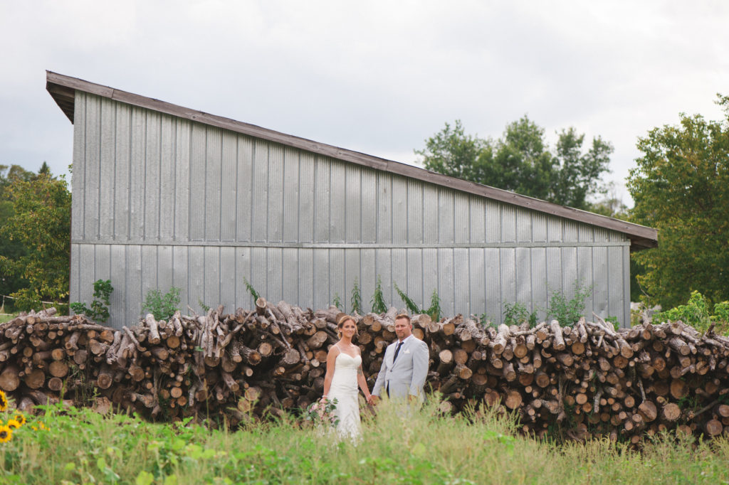 bride and groom in front of metal shed and stacks of wooden logs