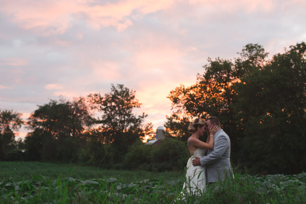 bride and groom in a field at sunset