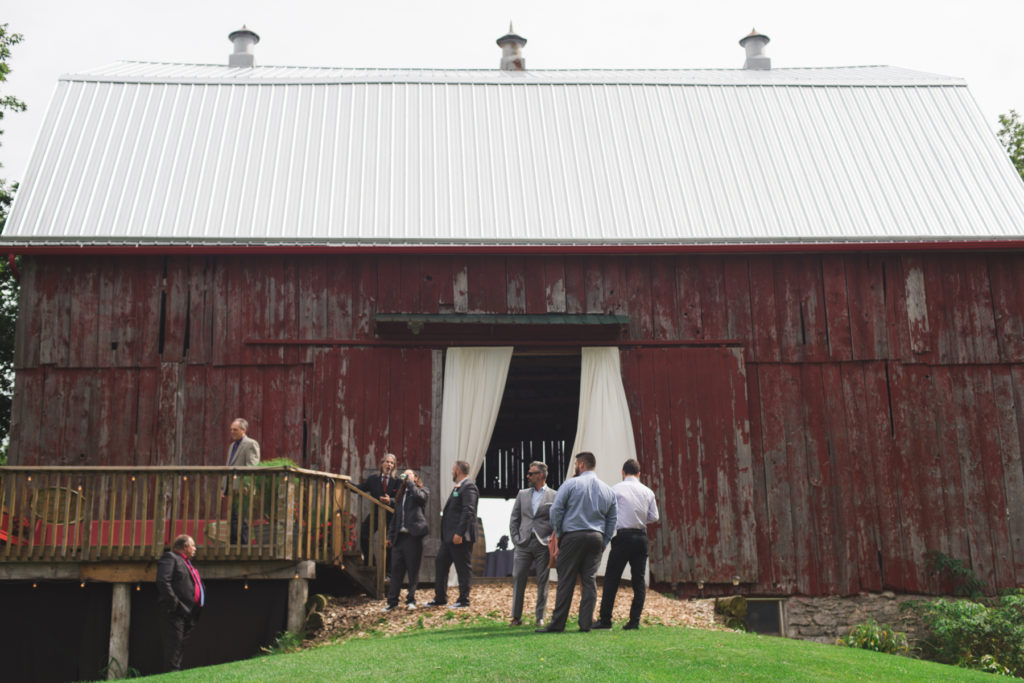 men standing outside red barn before wedding ceremony