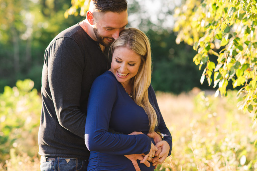 engaged couple expecting a baby cuddling in a field at sunset