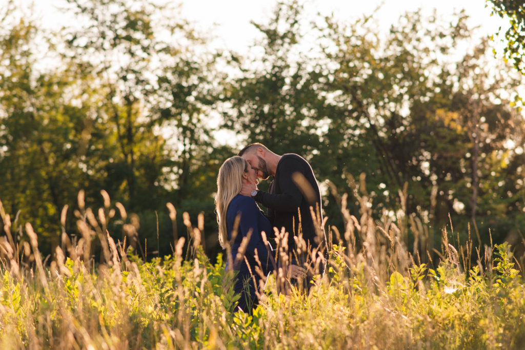 Engaged couple kissing in a field at sunset