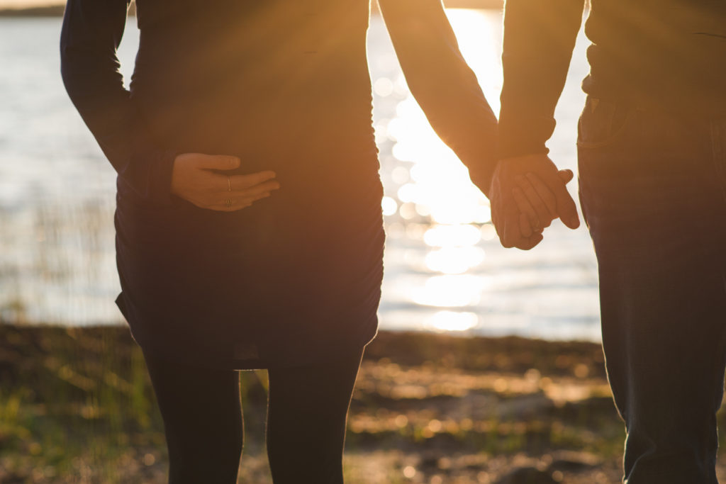 expecting parents holding hands and belly at sunset by the water