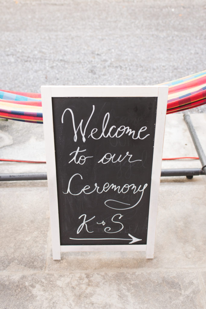 chalkboard signage in front of hammock at wedding ceremony