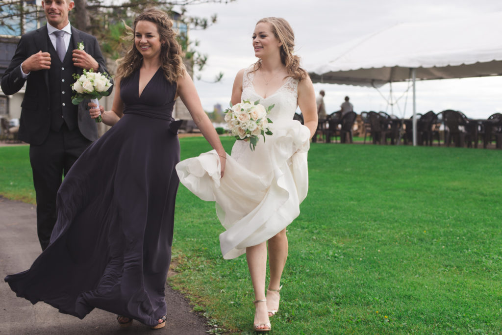 maid of honour holding bride's wedding dress as they walk