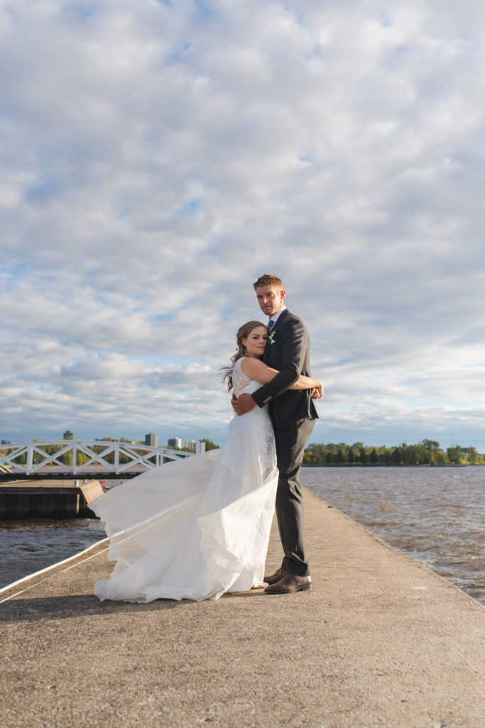 bride and groom standing on pier at sunset with wind blowing