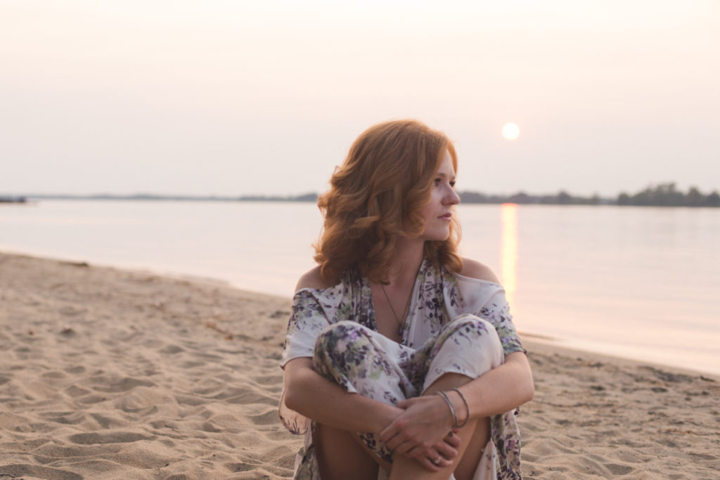 redhead girl sitting on the beach at sunset