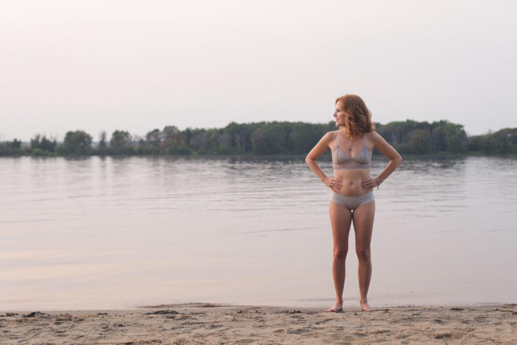 redhead girl standing by water's edge at sunset in her underwear