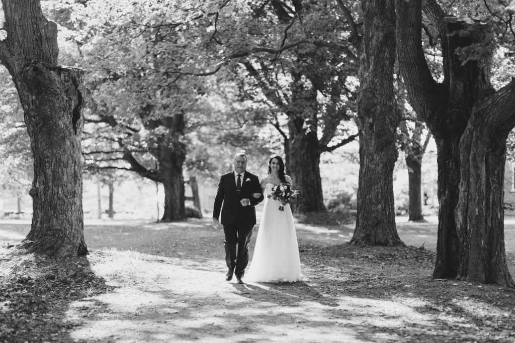 bride and her father walking down tree lined path towards ceremony