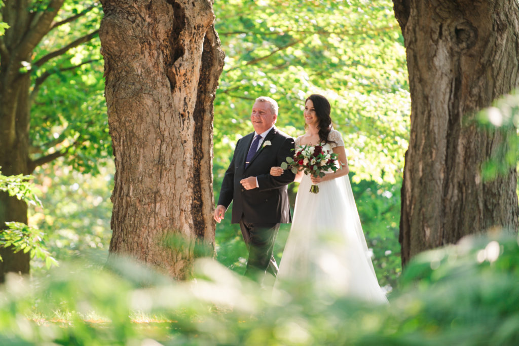 bride and her dad walking down tree lined path towards ceremony