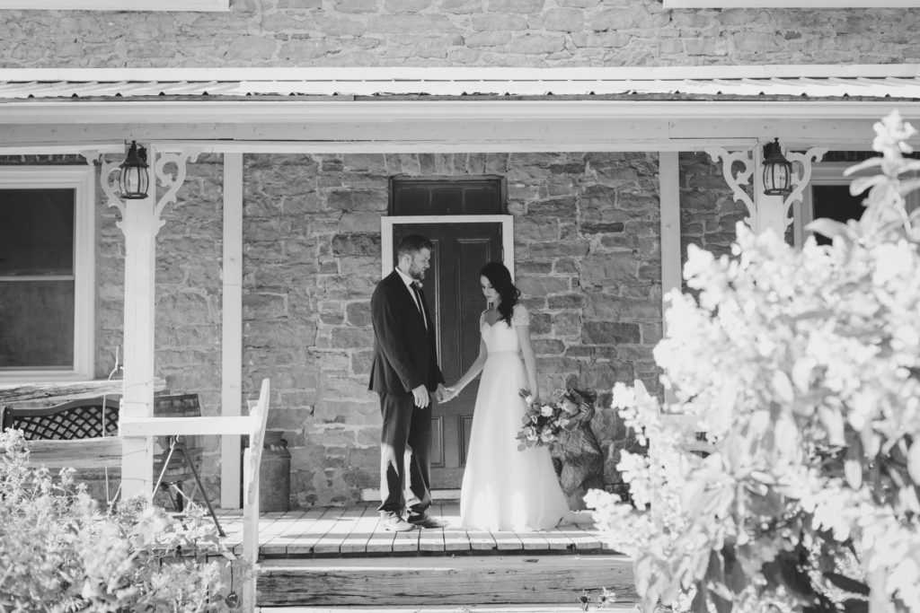 bride and groom standing on porch of old stone farmhouse