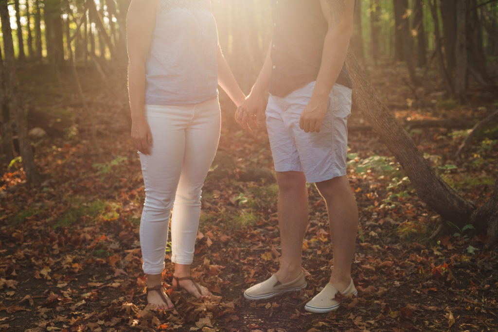 engaged couple holding hands in the forest at sunset