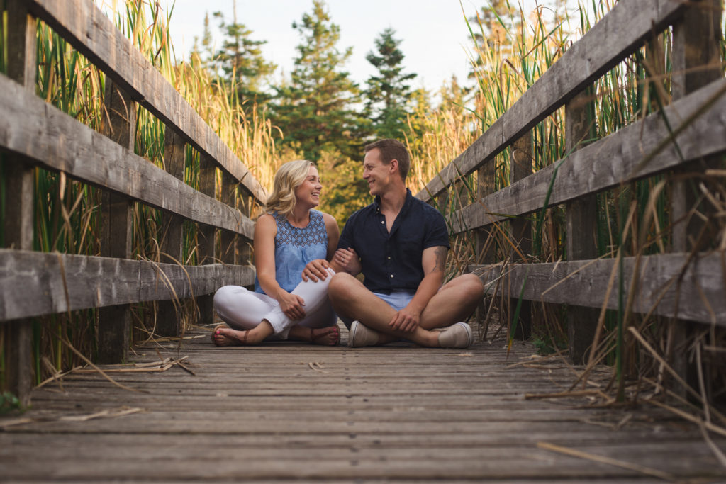 engaged couple sitting on a wooden bridge in the woods at sunset