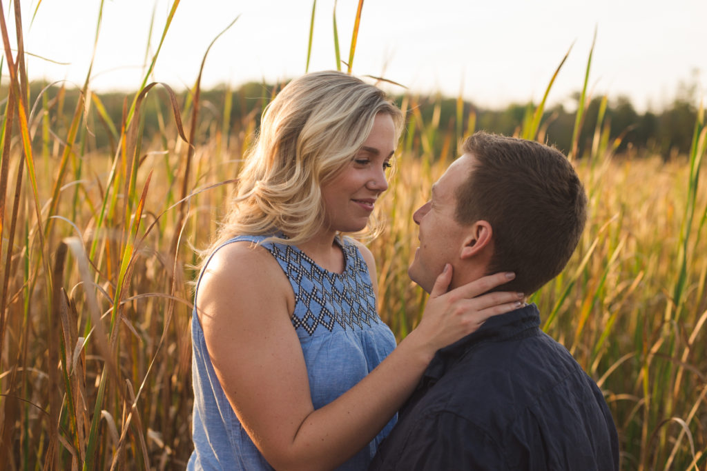 engaged couple smiling at each other at sunset in the tall grass