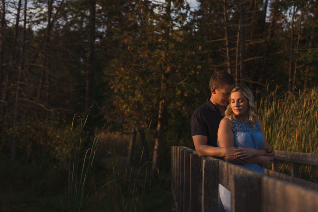 engaged couple cuddling on a wooden bridge at sunset
