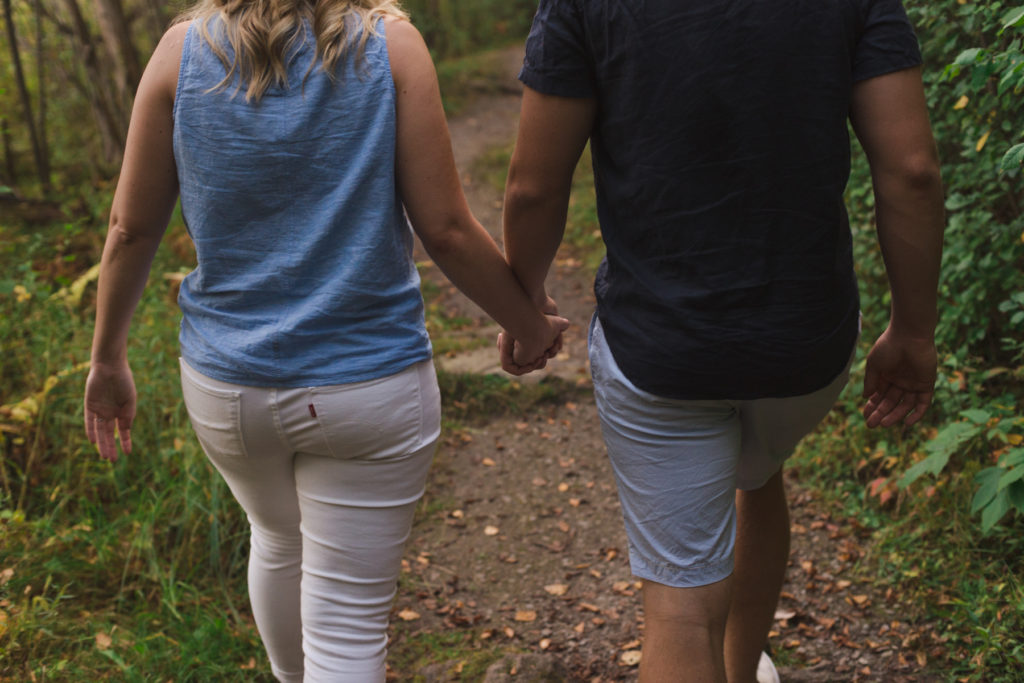 engaged couple walking along wooden trail holding hands