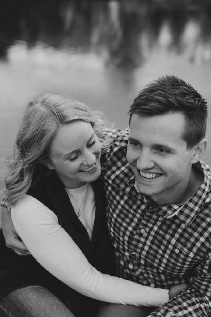 black and white photo of engaged couple laughing by the water
