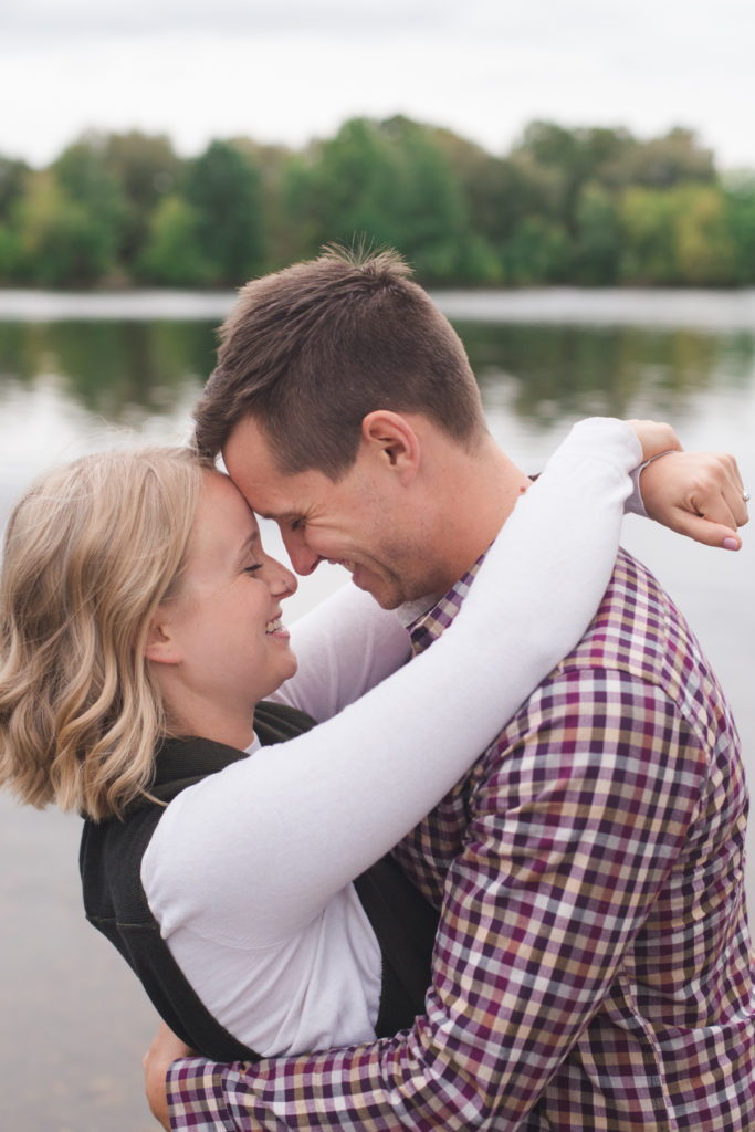 engaged couple hugging by the water with foreheads together