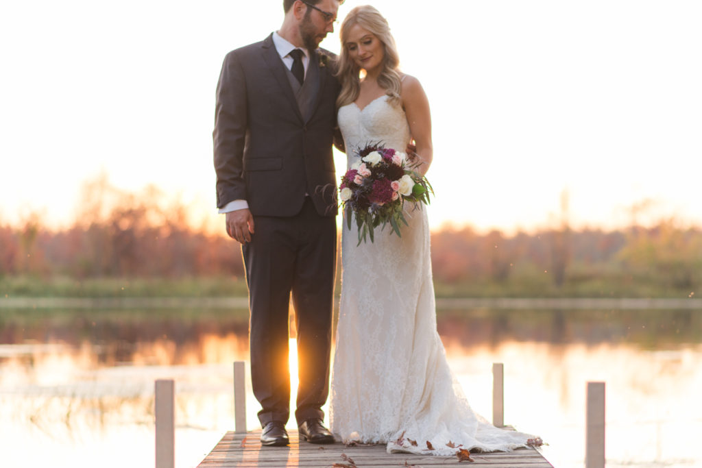 bride and groom standing on a dock at sunset