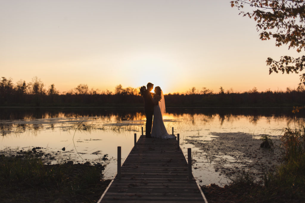 bride and groom standing at the end of a dock at sunset