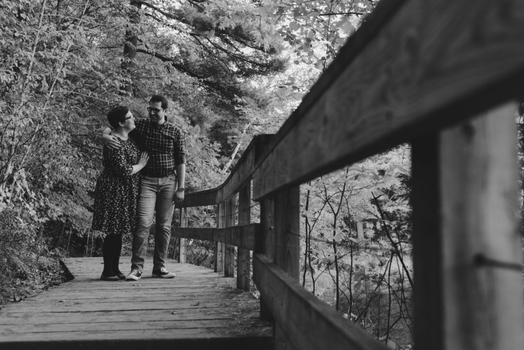 engaged couple standing along wooden trail laughing