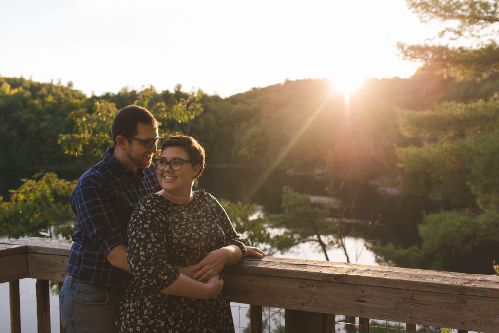 engaged couple smiling at sunset on lookout overtop of water