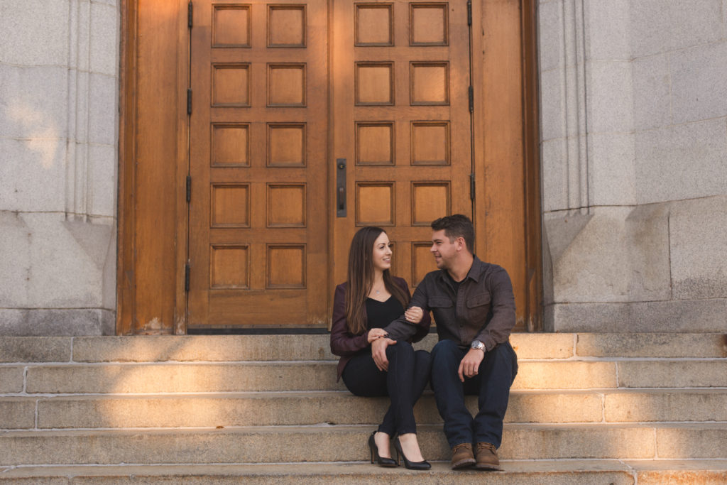 engaged couple sitting on steps in front of antique wooden doors