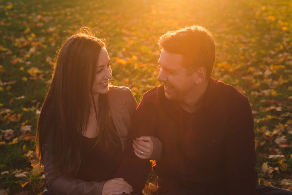 engaged couple sitting in the fall leaves at golden hour