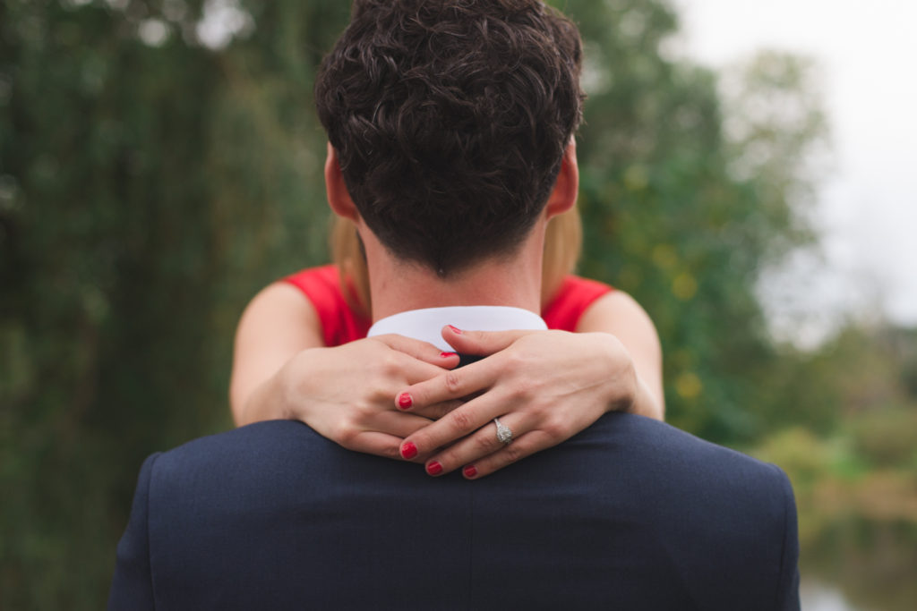 engaged girl wearing red nail polish with halo diamond ring around her fiancee's neck