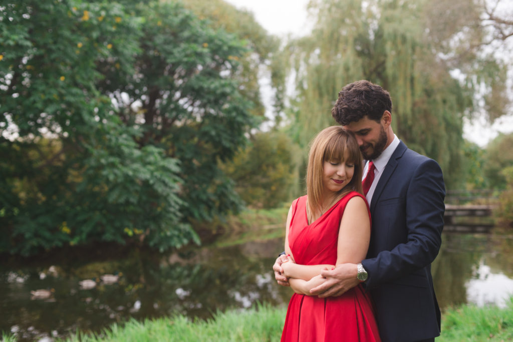 engaged couple cuddling by the pond with willow trees