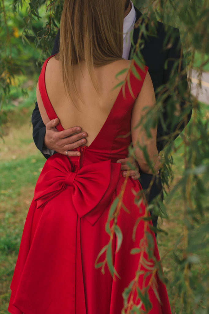 girl wearing a red dress with a big, red bow cuddling in the willow trees
