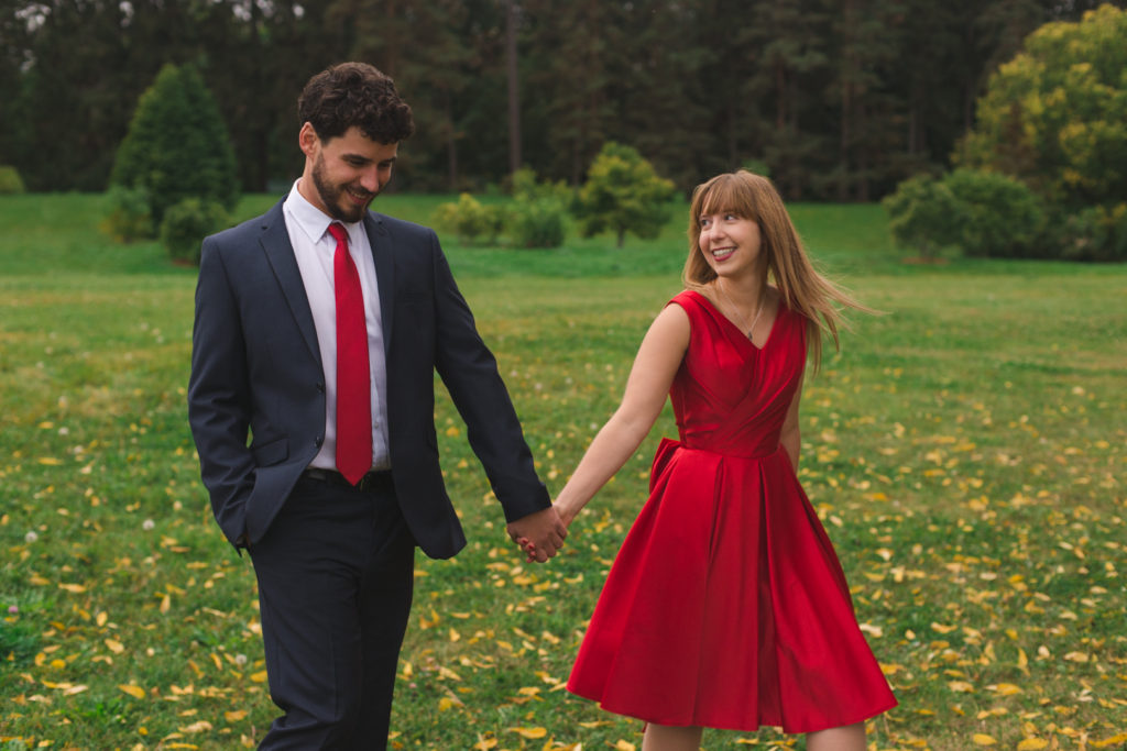 engaged couple in red walking among the trees