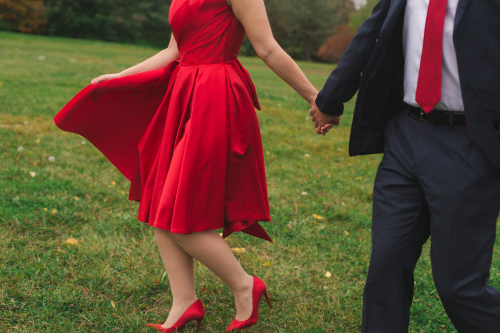 engaged couple holding hands, walking in the grass with dress flowing in the wind