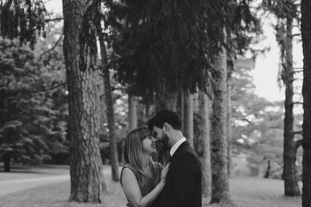 engaged couple cuddling underneath the trees in black and white