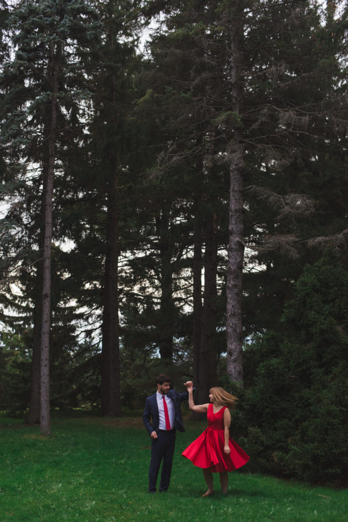 engaged couple wearing red dancing in the trees