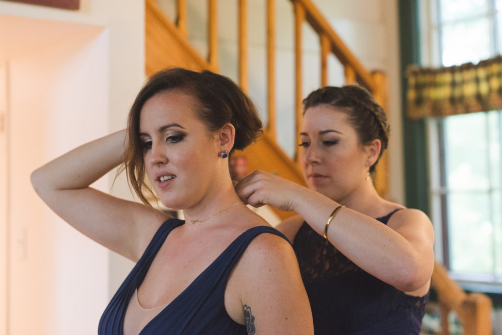 bridesmaid helping other bridesmaid tie up her necklace