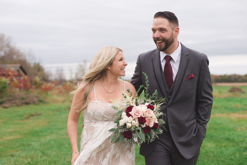 bride and groom laughing together as they walk through the fields of Strathmere