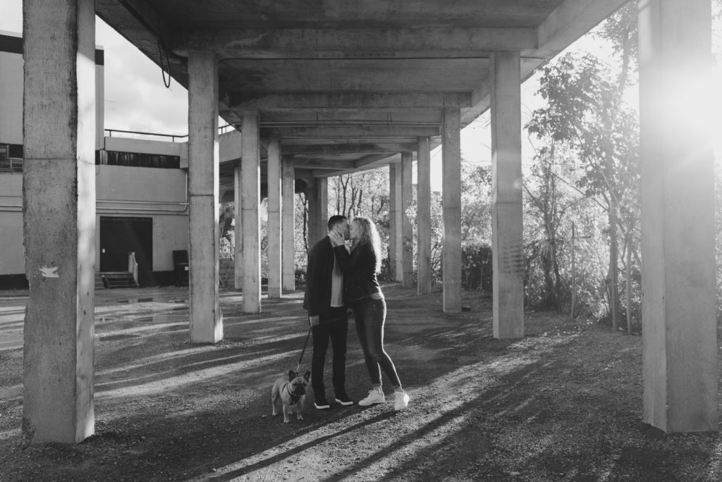 couple kissing under loading dock bridge at sunset