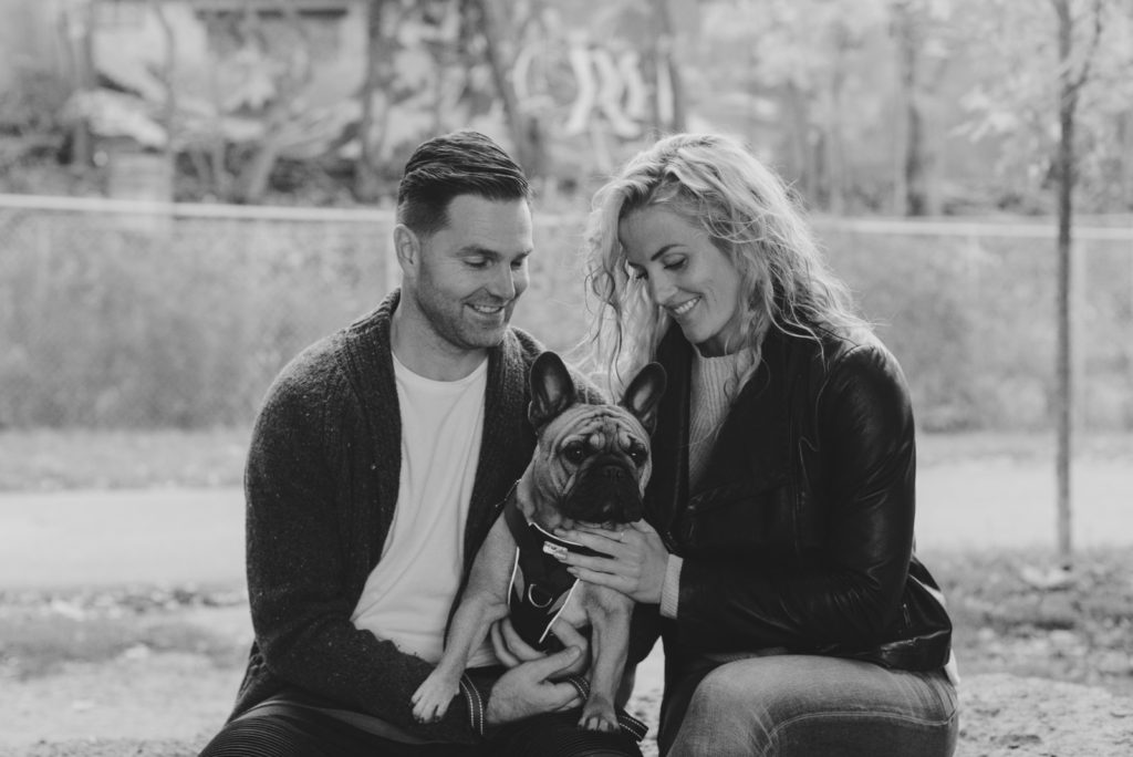 couple sitting on a rock smiling at their french bulldog